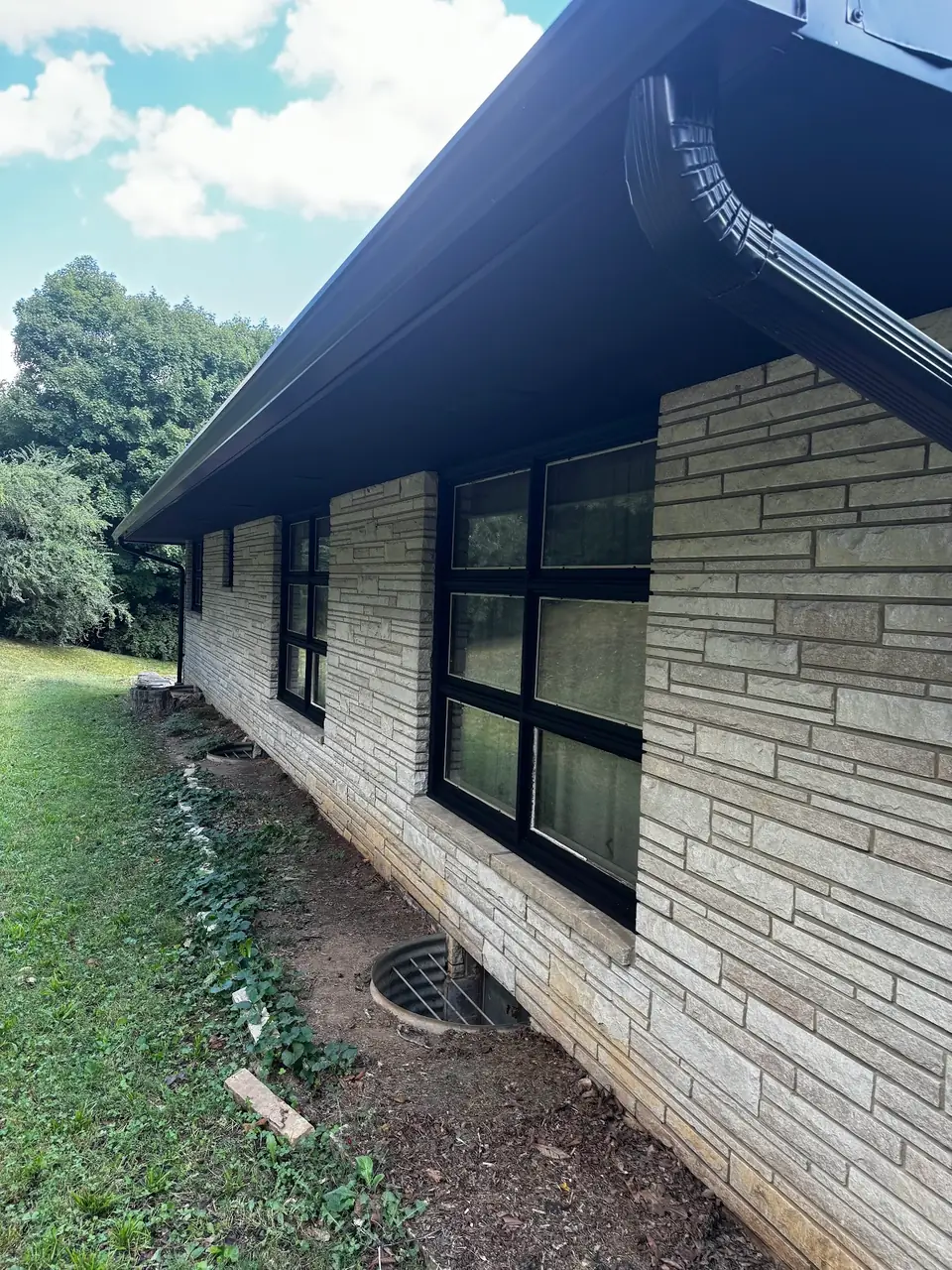 Black seamless gutters and downspout on a stone-veneer ranch home